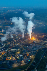 Aerial image of steel plant, factory, refinery with massive flame from chimney. Generating, producing steel and metal from coal and iron ore in IJmuiden Netherlands during evening alongside North Sea 