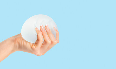 Female squeezing soft breast implant in hand on blue background.Plastic surgery, copy space