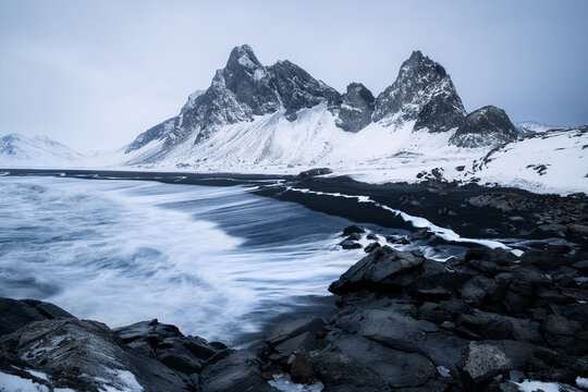 Moody stormy winter evening at Eystrahorn mountain viewpoint in Iceland, with snow covering the mountain and raging waves from Atlantic Ocean