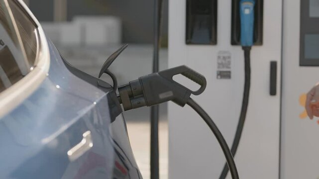 An unidentifiable man removing the charger from an electric vehicle at a modern charging station, emphasizing sustainable and green transportation options in urban settings.