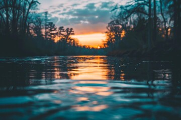 The sunset reflecting off the surface of a calm river, with a softly blurred background of surrounding trees and sky. 