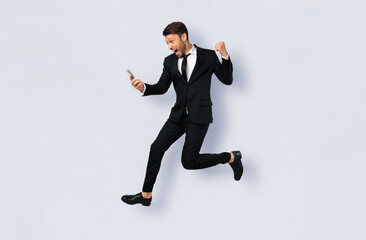 A man in a suit jumps in the air while looking at his phone with a surprised expression.