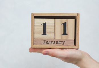 Woman's hand holds wooden block calendar with the date January 11 on white concrete background