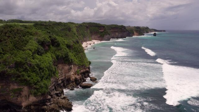 Aerial view of serene beach with ocean waves, rocks, and cliffs, Mbawana Beach, Sumba Island, Indonesia.