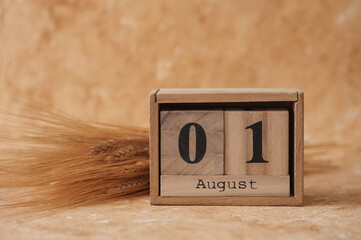 Wooden block calendar with the date August 01 and spikelets of wheat on a beige concrete background