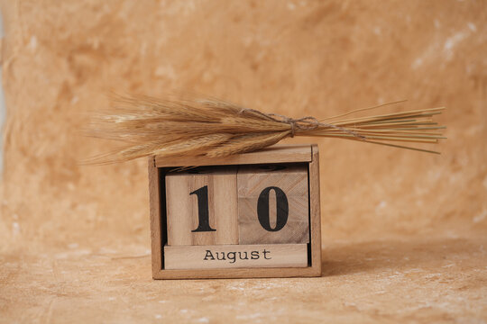 Wooden block calendar with the date August 10 and spikelets of wheat on a beige concrete background