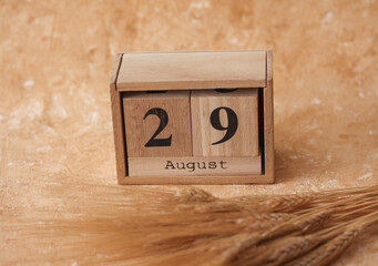 Wooden block calendar with the date August 29 and spikelets of wheat on a beige concrete background