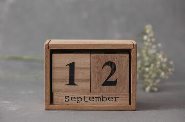 Wooden calendar with the date September 12 and gypsophila flowers on a gray concrete background