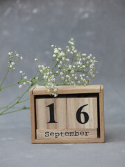 Wooden calendar with the date September 16 and gypsophila flowers on a gray concrete background