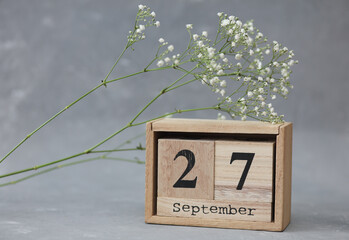 Wooden calendar with the date September 27 and gypsophila flowers on a gray concrete background