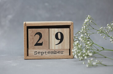 Wooden calendar with the date September 29 and gypsophila flowers on a gray concrete background