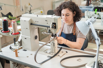 A woman tanner sews a leather belt on a sewing machine. 