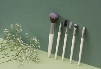 Set of makeup brushes and gypsophila flowers on a green background