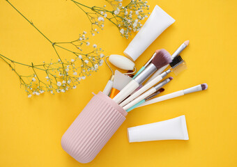 Organizer case with makeup accessories and flowers on yellow background