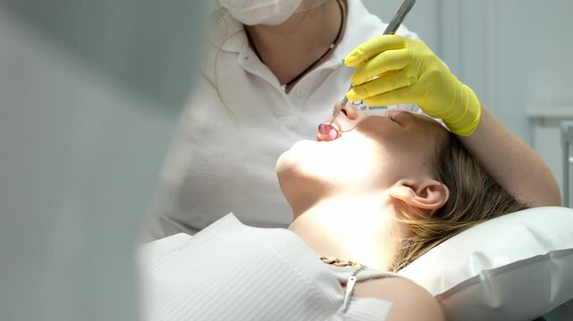 Dentist filling. female dentist examining young girl patient's teeth at dental clinic. Doctor probing teeth with dental instrument using an explorer look for cavities treatment and checking