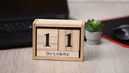 Wooden calendar with the date October 11 on a desktop with a laptop