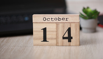 Wooden calendar with the date October 14 on desktop with laptop