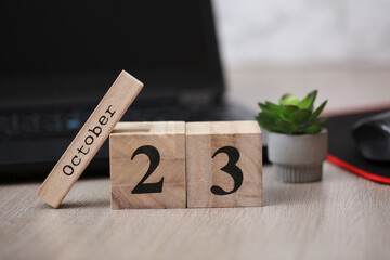 Wooden calendar with the date October 23 on desktop with laptop