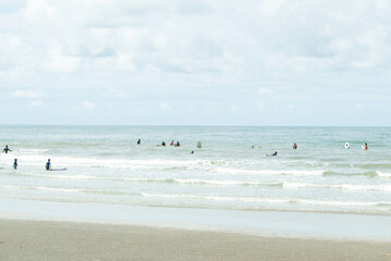 People and tourists surfing Board in blue sea and white beach. Landscape nature view of beautiful tropical beach and sea in sunny day. White, brown clean beach. Distant view of mountain of island.