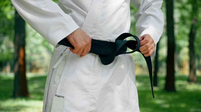close up outdoors in the park in sunny weather a young karate guy tightens his belt using the karate technique martial arts black belt healthy lifestyle