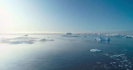 Icebergs ice floes drift polar ocean in Antarctica. Wild nature arctic winter landscape. Global warming, climate change, melting ice. Panoramic aerial drone flight over frozen sea under blue sky