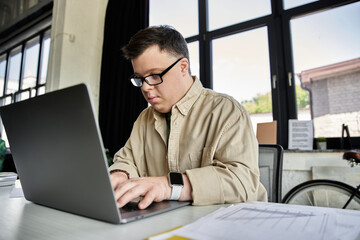 A young man with Down syndrome focuses intently on his work while typing on a laptop.