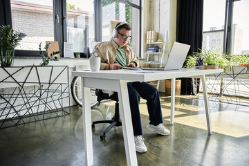 A young man with Down syndrome sits at a desk in an office, working on a laptop.