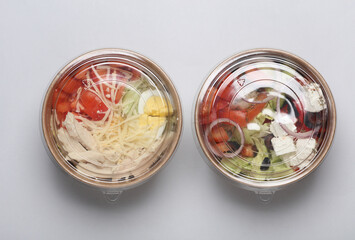 Greek and Caesar salad in disposable cardboard containers on a gray background