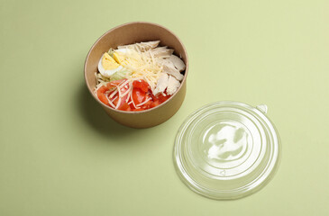 Caesar salad in a disposable cardboard container on green background