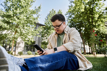 A man with Down syndrome relaxes on the grass, enjoying a moment on his phone.