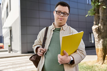 A man with Down syndrome holds a yellow folder while walking outside a building.