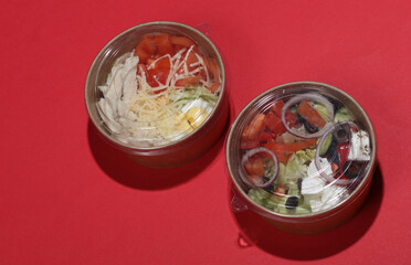 Greek and Caesar salad in disposable cardboard containers on red background