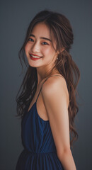 Fototapeta premium Beautiful Japanese woman with long hair wearing makeup and smiling while dressed in a blue dress with a simple background.
