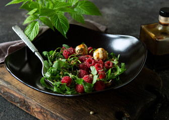bowl with salad of arugula, raspberries and goat cheese chevre on a dark table