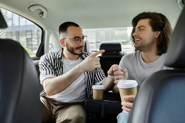 Two men, holding hands and enjoying coffee, converse in the backseat of a car.