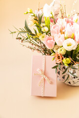 Beautiful bouquet of rose and tulips flowers and pink gift box on beige pastel background. Floral arrangement. Gift for holiday, birthday, Wedding, Mother's Day, Valentine's day, Women's Day.