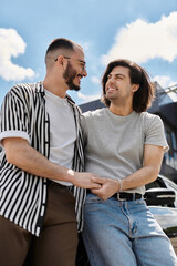 Two men, holding hands, laugh and gaze at each other as they walk together through a city.