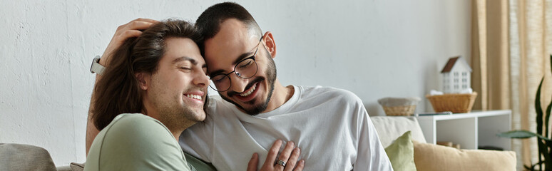 Obraz premium Two men embrace on a couch, smiling and laughing together.