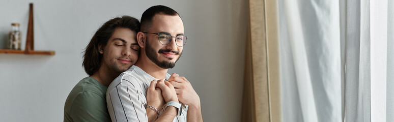 A loving gay couple embraces in a moment of intimacy by a window.