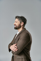 Obraz premium A sophisticated man with a beard, dressed in elegant attire, stands with arms crossed against a grey background.