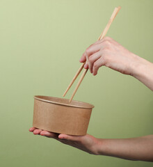 Hands holding a package of takeaway food with Chinese chopsticks on a green background