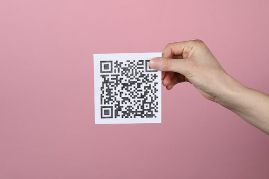 Hand holding a piece of paper with a quar code on a pink background