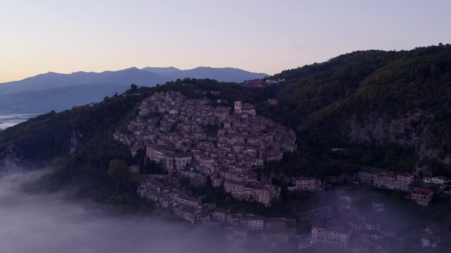 Aerial view of misty Santo Stefano church and town amidst mountain fog, Artena, Italy.