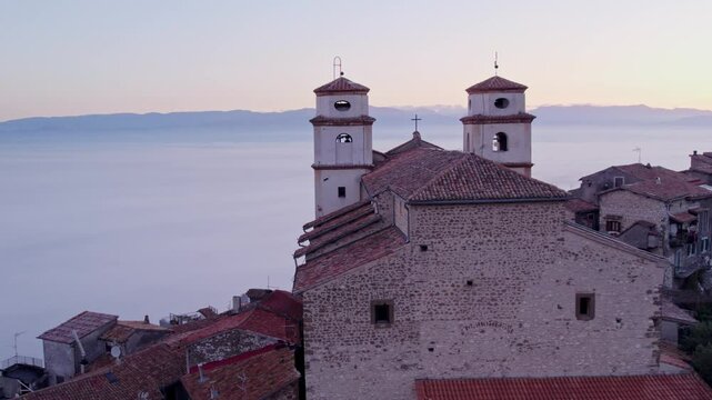 Aerial view of Santo Stefano church in sunrise with fog and mountain backdrop, Artena, Italy.