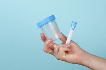 Hand holding empty blood test tube and Urine test jar on a blue background