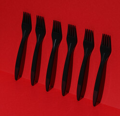 Black plastic forks on a red background with shadow. Creative layout