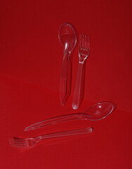 Plastic transparent spoons and forks on a red background