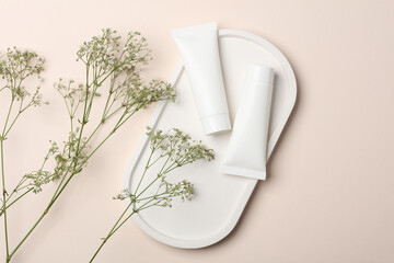 White cream tubes in gypsum oval plate with gypsophila flowers on beige background