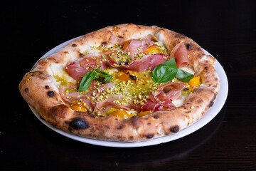 Pizza tradizionale gourmet napoletana con mozzarella, prosciutto crudo pomodori gialli, pesto di pistacchio, granella di pistacchio e basilico fresco servita in una pizzeria