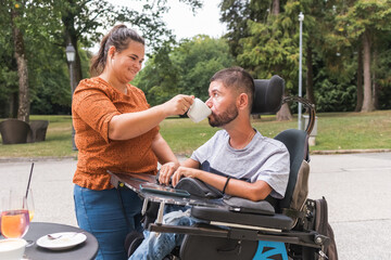 Girlfriend assisting her boyfriend with physical disability drinking coffee in a cafe. Love and conquering adversity concepts.